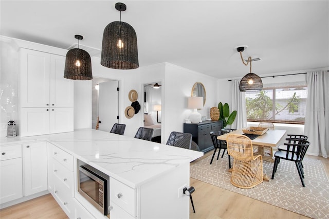 404 Bayshore Rd, Nokomis, FL 34275 - kitchen featuring stainless steel microwave, a peninsula, light wood-type flooring, white cabinets, and light stone counters