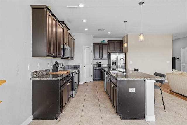 1234 Harbour Blue St, Ruskin, FL 33570 - kitchen featuring appliances with stainless steel finishes, a kitchen bar, light tile patterned floors, dark brown cabinets, and dark stone counters