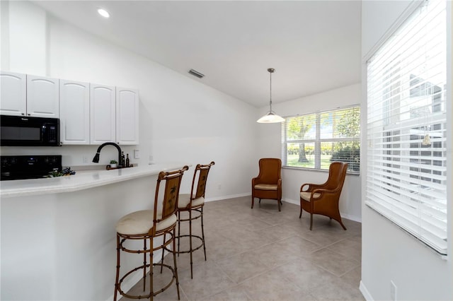 2199 Palm Ct, North Port, FL 34287 - kitchen featuring black microwave, lofted ceiling, stove, white cabinetry, and a breakfast bar area