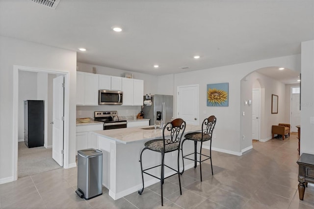 2105 Grand Flora Trl, Bradenton, FL 34208 - kitchen featuring stainless steel appliances, arched walkways, a center island with sink, a breakfast bar area, and white cabinets