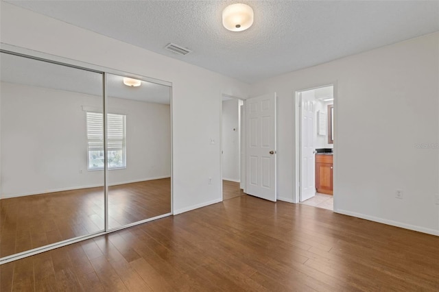 5356 Royal Palm Ave Unit 5356, Sarasota, FL 34234 - unfurnished bedroom featuring wood finished floors, a closet, baseboards, a textured ceiling, and connected bathroom