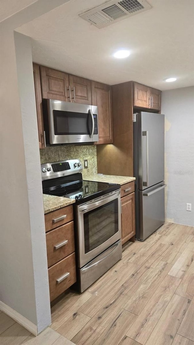 5325 Murdock Ave, Sarasota, FL 34231 - kitchen featuring appliances with stainless steel finishes, light wood-style flooring, brown cabinets, tasteful backsplash, and light stone counters