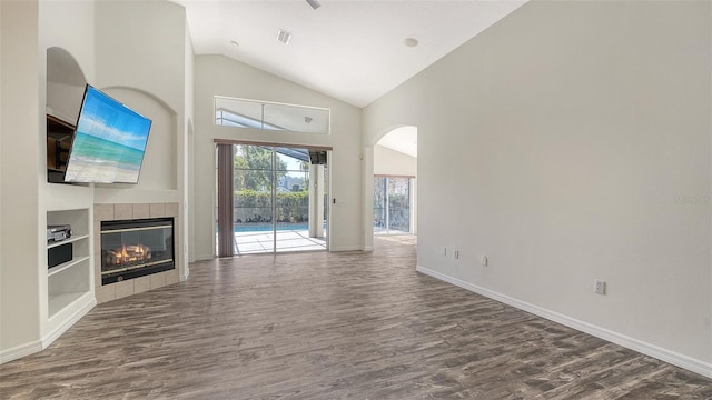 6213 Willet Ct, Lakewood Ranch, FL 34202 - unfurnished living room featuring dark wood-style flooring, arched walkways, high vaulted ceiling, baseboards, and a tile fireplace