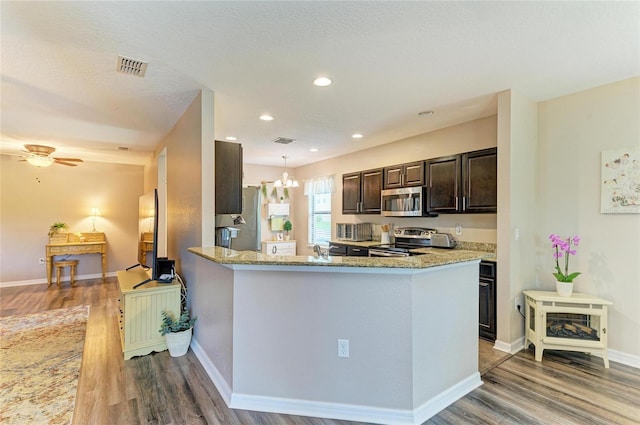 7410 61st St E, Palmetto, FL 34221 - kitchen with appliances with stainless steel finishes, wood finished floors, dark brown cabinetry, light stone counters, and a chandelier