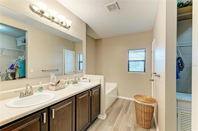 7410 61st St E, Palmetto, FL 34221 - bathroom featuring double vanity, a walk in closet, a bath, wood finished floors, and a textured ceiling
