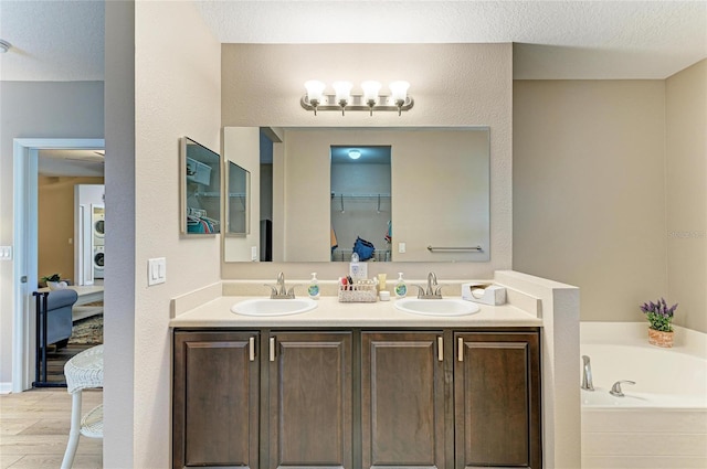 7410 61st St E, Palmetto, FL 34221 - bathroom featuring double vanity, stacked washing machine and dryer, a garden tub, wood finished floors, and a chandelier