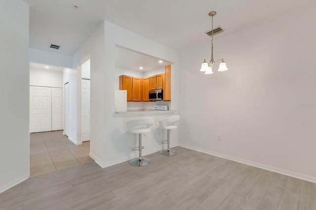 3402 Parkridge Cir, Sarasota, FL 34243 - kitchen with stainless steel microwave, freestanding refrigerator, a kitchen bar, a chandelier, and light wood-type flooring