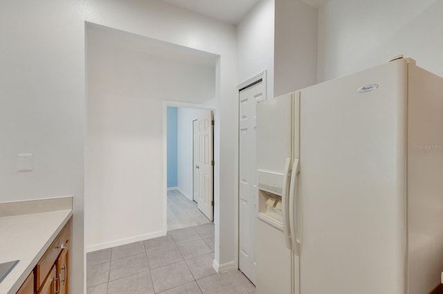 3402 Parkridge Cir, Sarasota, FL 34243 - kitchen with white refrigerator with ice dispenser, light tile patterned floors, light countertops, brown cabinets, and baseboards
