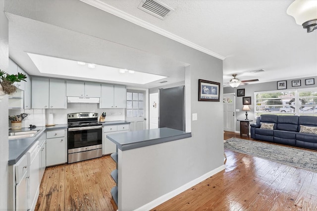 304 34th St W, Bradenton, FL 34205 - kitchen with stainless steel range with electric cooktop, dark countertops, light wood-type flooring, baseboards, and a skylight