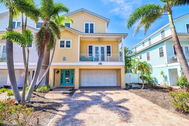 145 50th St, Holmes Beach, FL 34217 - coastal inspired home featuring french doors, a balcony, decorative driveway, a garage, and a ceiling fan