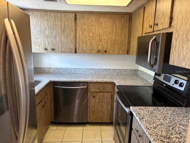 10800 N US Highway 19 Unit 237, Pinellas Park, FL 33782 - kitchen with stainless steel appliances, light tile patterned floors, brown cabinetry, and light stone counters