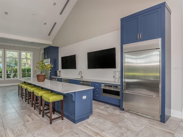 12682 Shimmering Oak Cir, Venice, FL 34293 - kitchen with stainless steel appliances, blue cabinetry, a breakfast bar, high vaulted ceiling, and a kitchen island