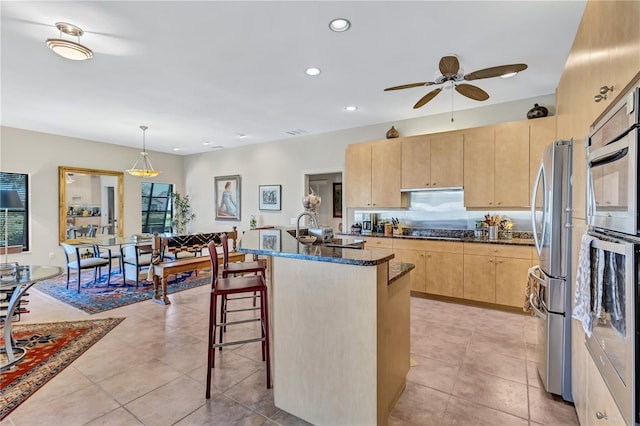 105 Inlets Blvd Unit 105, Nokomis, FL 34275 - kitchen with light brown cabinetry, dark stone countertops, ceiling fan, appliances with stainless steel finishes, and a kitchen breakfast bar