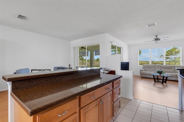 9402 71st Ave E, Palmetto, FL 34221 - kitchen with a ceiling fan, a center island, open floor plan, dark stone counters, and brown cabinets