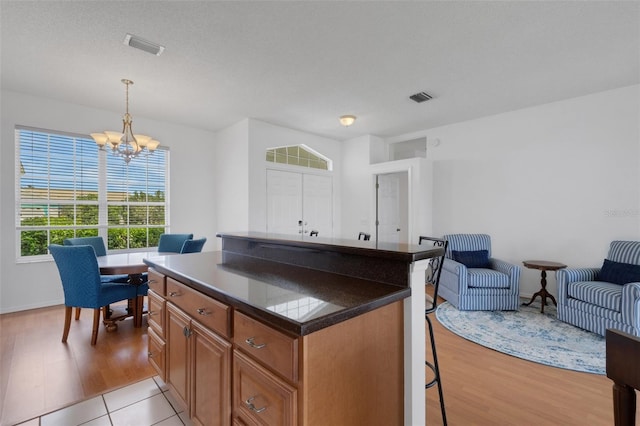 9402 71st Ave E, Palmetto, FL 34221 - kitchen with a chandelier, dark countertops, brown cabinetry, a kitchen breakfast bar, and light wood finished floors