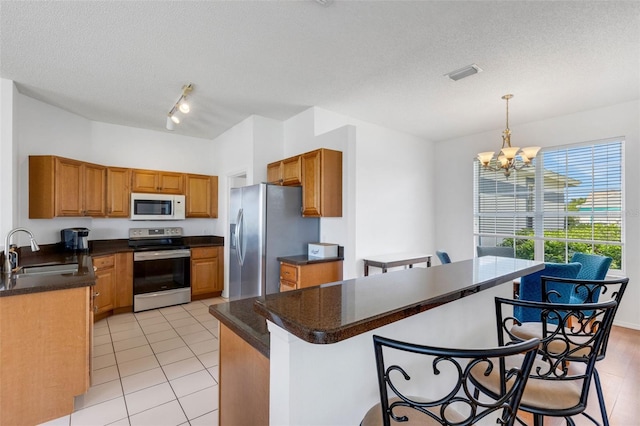 9402 71st Ave E, Palmetto, FL 34221 - kitchen with stainless steel appliances, a sink, a breakfast bar area, brown cabinetry, and a textured ceiling