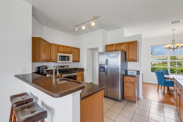 9402 71st Ave E, Palmetto, FL 34221 - kitchen with stainless steel appliances, a chandelier, a kitchen breakfast bar, a peninsula, and brown cabinets