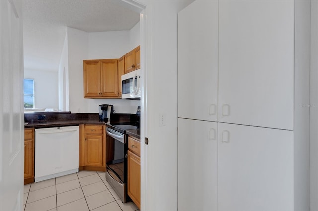 9402 71st Ave E, Palmetto, FL 34221 - kitchen featuring white appliances, dark countertops, light tile patterned floors, and brown cabinets