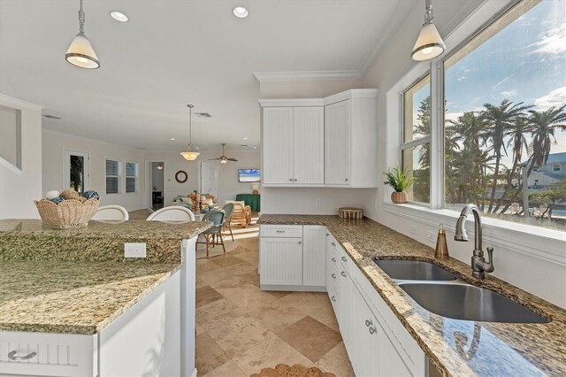 634 Key Royale Dr, Holmes Beach, FL 34217 - kitchen featuring a sink, white cabinets, light stone counters, a ceiling fan, and ornamental molding
