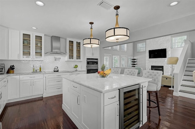 13514 4th Plz E, Bradenton, FL 34212 - kitchen with beverage cooler, wall chimney exhaust hood, stainless steel double oven, a kitchen island, and decorative backsplash