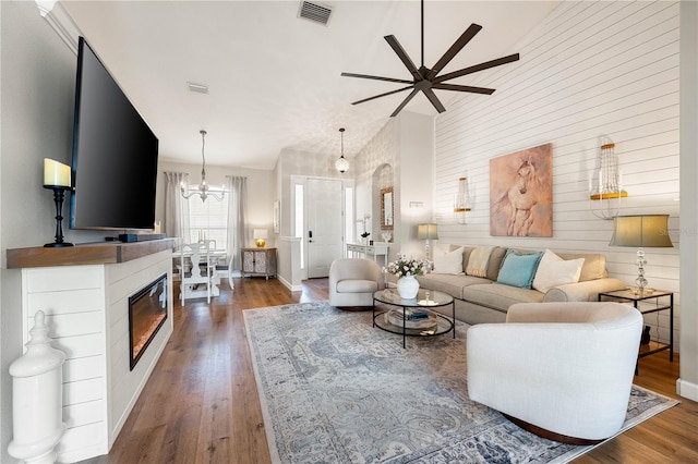 6750 64th Ter E, Bradenton, FL 34203 - living area with a ceiling fan, wood finished floors, a chandelier, wooden walls, and a glass covered fireplace
