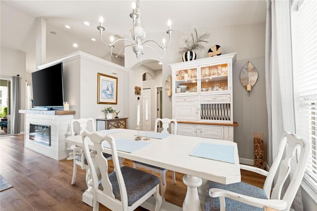 6750 64th Ter E, Bradenton, FL 34203 - dining space featuring a chandelier, light wood-type flooring, arched walkways, a glass covered fireplace, and high vaulted ceiling