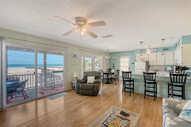 1103 Shore View Dr, Englewood, FL 34223 - living room featuring ceiling fan, a textured ceiling, light wood-style flooring, and a water view