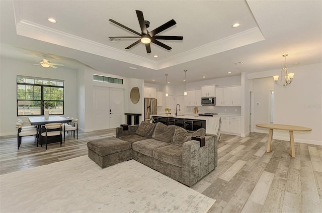 2546 Malibu Ln, North Port, FL 34286 - living room with a raised ceiling, a ceiling fan, light wood-style floors, a chandelier, and ornamental molding