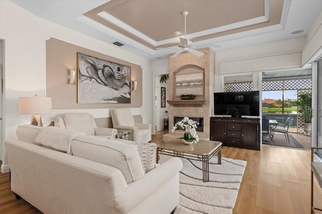 7513 Coventry Ct, Lakewood Ranch, FL 34202 - living room with a raised ceiling, light wood finished floors, a ceiling fan, a premium fireplace, and crown molding