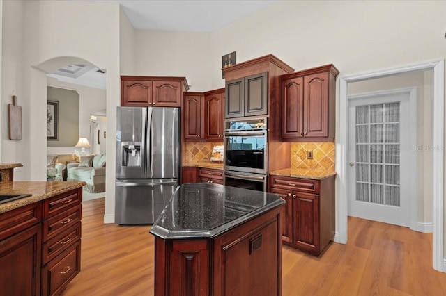 7513 Coventry Ct, Lakewood Ranch, FL 34202 - kitchen featuring appliances with stainless steel finishes, light wood-style floors, arched walkways, decorative backsplash, and dark stone countertops