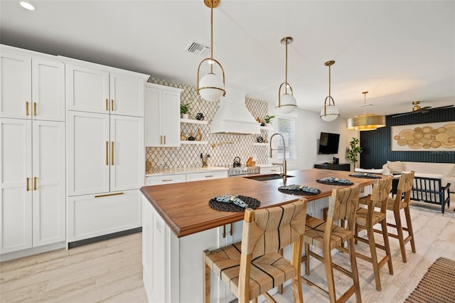109 Palmetto Ave, Anna Maria, FL 34216 - kitchen featuring a sink, light wood-style flooring, an island with sink, white cabinetry, and decorative light fixtures