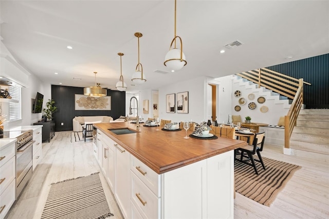 109 Palmetto Ave, Anna Maria, FL 34216 - kitchen with a sink, butcher block counters, stainless steel range, an accent wall, and white cabinetry