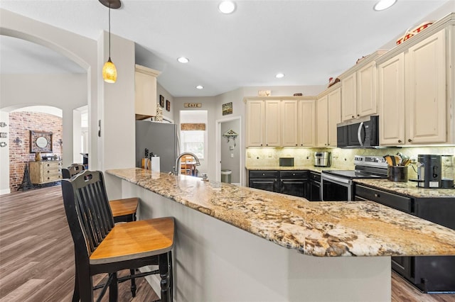 743 Stonecrest Dr, Sarasota, FL 34232 - kitchen featuring stainless steel appliances, arched walkways, wood finished floors, light stone countertops, and recessed lighting