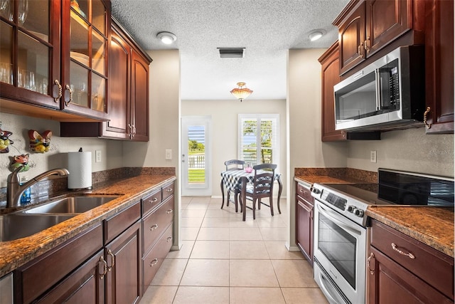 4194 Banbury Cir, Parrish, FL 34219 - kitchen with stainless steel appliances, a sink, glass insert cabinets, light tile patterned floors, and a textured ceiling