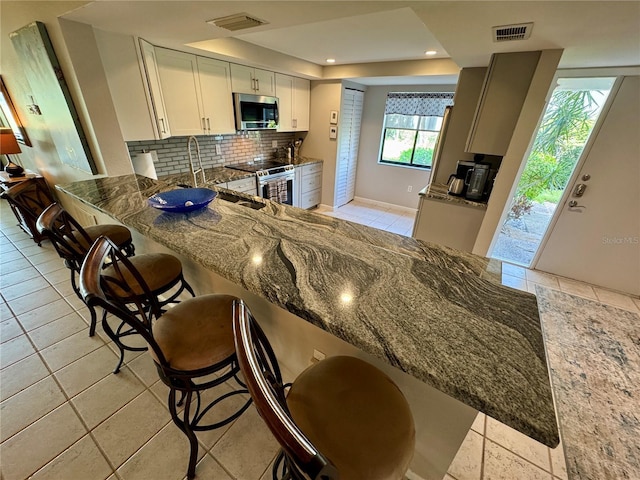 3500 El Conquistador Pkwy Unit 347, Bradenton, FL 34210 - kitchen with stainless steel appliances, dark stone countertops, tasteful backsplash, a raised ceiling, and a breakfast bar