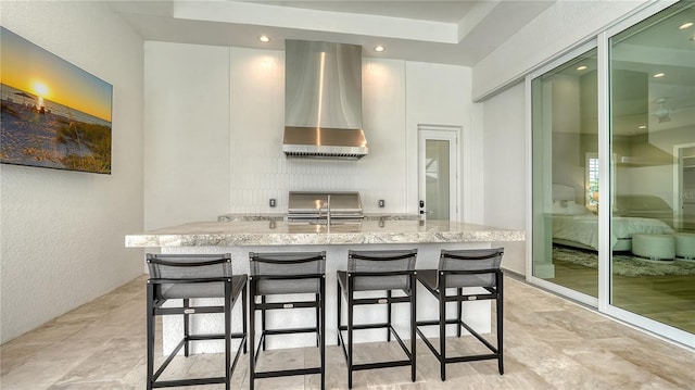 8537 Pavia Way, Bradenton, FL 34202 - kitchen featuring wall chimney exhaust hood, light stone counters, a kitchen island with sink, a breakfast bar, and stove
