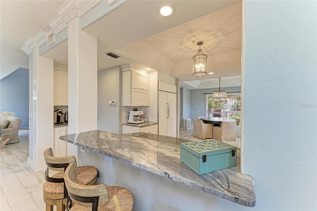 8963 Fishermens Bay Dr, Sarasota, FL 34231 - kitchen with white cabinets, a breakfast bar, stone countertops, paneled built in refrigerator, and backsplash