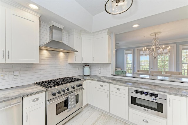 8963 Fishermens Bay Dr, Sarasota, FL 34231 - kitchen with wall chimney range hood, high end stove, a chandelier, white cabinets, and ornamental molding