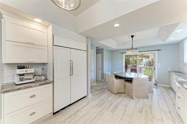 8963 Fishermens Bay Dr, Sarasota, FL 34231 - kitchen featuring a raised ceiling, decorative backsplash, white cabinetry, hanging light fixtures, and light stone counters