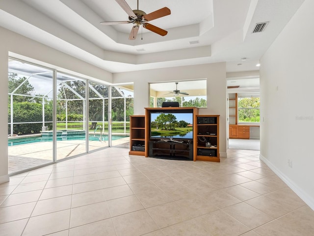 6811 Honeysuckle Trl, Lakewood Ranch, FL 34202 - unfurnished living room featuring a ceiling fan, a tray ceiling, tile patterned floors, a sunroom, and plenty of natural light