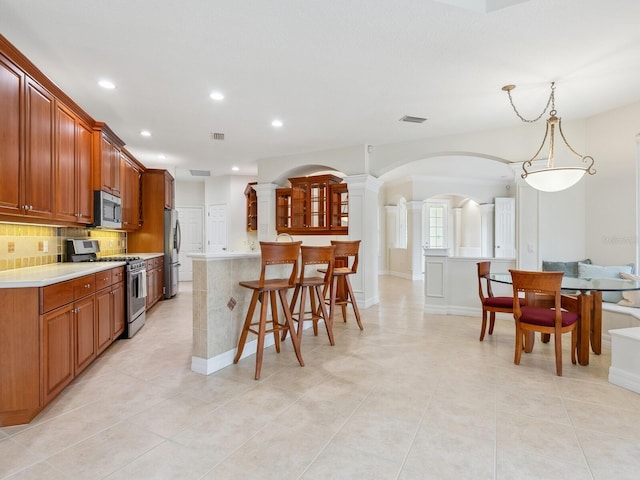6811 Honeysuckle Trl, Lakewood Ranch, FL 34202 - kitchen with stainless steel appliances, a breakfast bar, light countertops, recessed lighting, and ornate columns