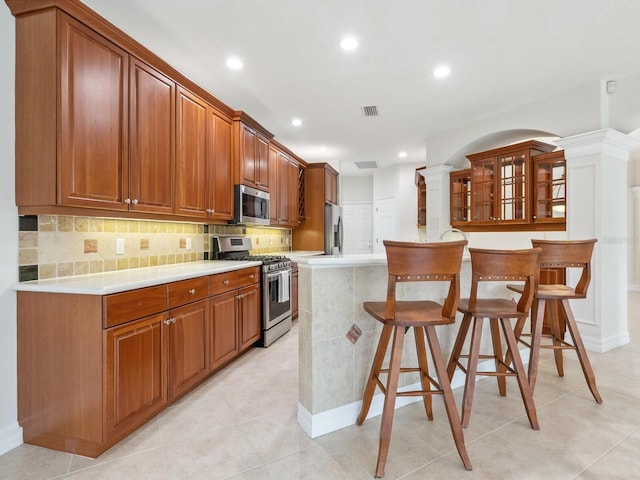 6811 Honeysuckle Trl, Lakewood Ranch, FL 34202 - kitchen with appliances with stainless steel finishes, decorative columns, a breakfast bar area, recessed lighting, and brown cabinetry