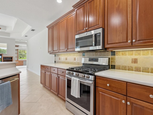 6811 Honeysuckle Trl, Lakewood Ranch, FL 34202 - kitchen featuring stainless steel appliances, light tile patterned flooring, decorative backsplash, a tray ceiling, and light countertops