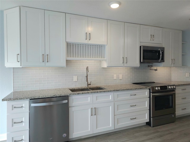 5207 86th Street Ct W, Bradenton, FL 34210 - kitchen with stainless steel appliances, a sink, white cabinets, light stone counters, and decorative backsplash