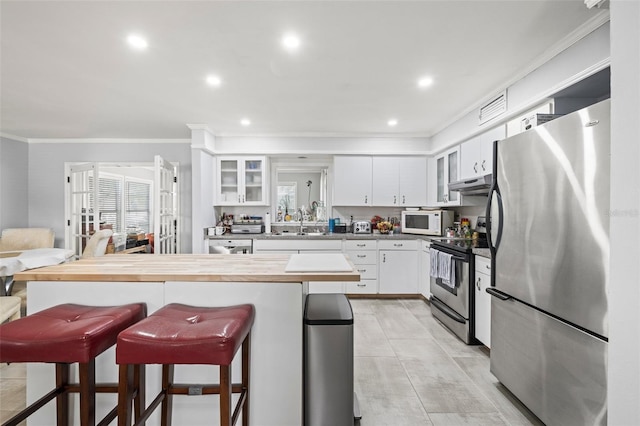 2204 67th St W, Bradenton, FL 34209 - kitchen with stainless steel appliances, ornamental molding, a kitchen bar, under cabinet range hood, and white cabinetry