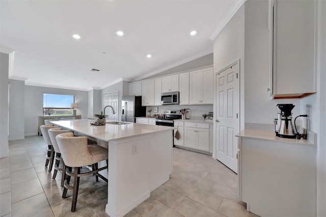 5695 Palmer Cir Unit 203, Bradenton, FL 34211 - kitchen with stainless steel appliances, crown molding, a breakfast bar area, white cabinets, and a center island with sink