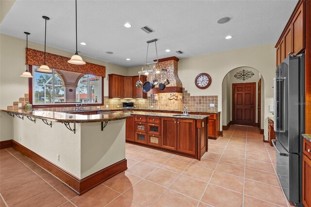 7025 Saddle Creek Cir, Sarasota, FL 34241 - kitchen with high end refrigerator, brown cabinetry, a kitchen bar, backsplash, and recessed lighting