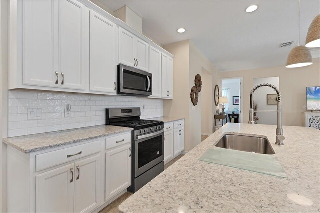 4524 Baltry Ct, Bradenton, FL 34211 - kitchen with stainless steel appliances, a sink, white cabinetry, decorative backsplash, and decorative light fixtures