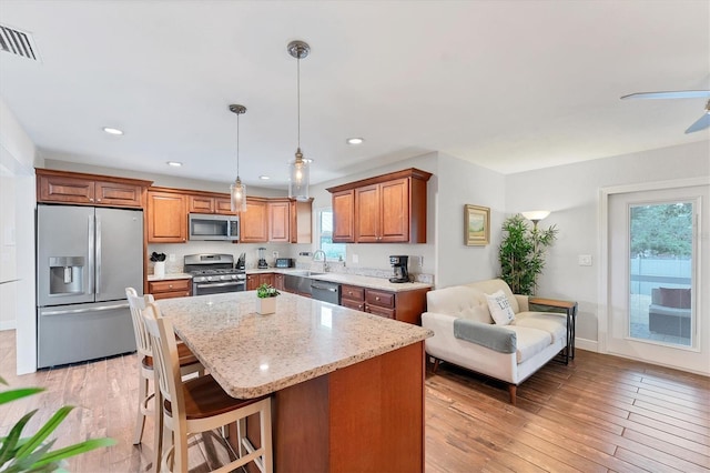7727 9th Avenue Dr NW, Bradenton, FL 34209 - kitchen with appliances with stainless steel finishes, light stone counters, brown cabinets, a sink, and a center island
