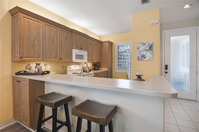 8579 54th Avenue Cir E, Bradenton, FL 34211 - kitchen featuring white appliances, light countertops, a breakfast bar, a peninsula, and light tile patterned flooring
